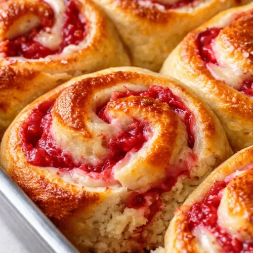 Soft gooey strawberry shortcake cheesecake rolls drizzled with strawberry glaze on a white plate